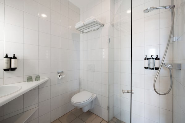 A modern bathroom with a toilet, a glass-enclosed shower, and a sink with toiletries. - Hotel Hoogeerd by Flow (Niftrik)