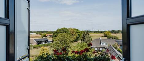 Blick aus einem Fenster auf eine ländliche Landschaft mit Häusern, Bäumen und wolkenlosem Himmel.