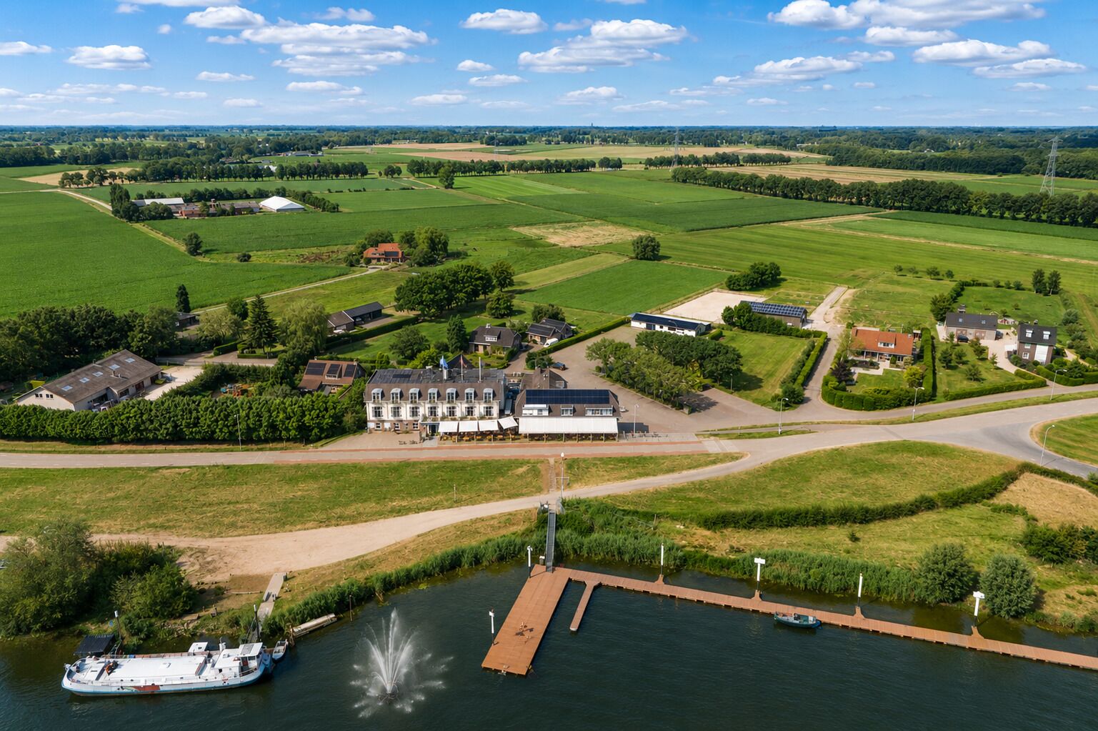 A riverside property with a large building, a dock, and surrounding green fields.