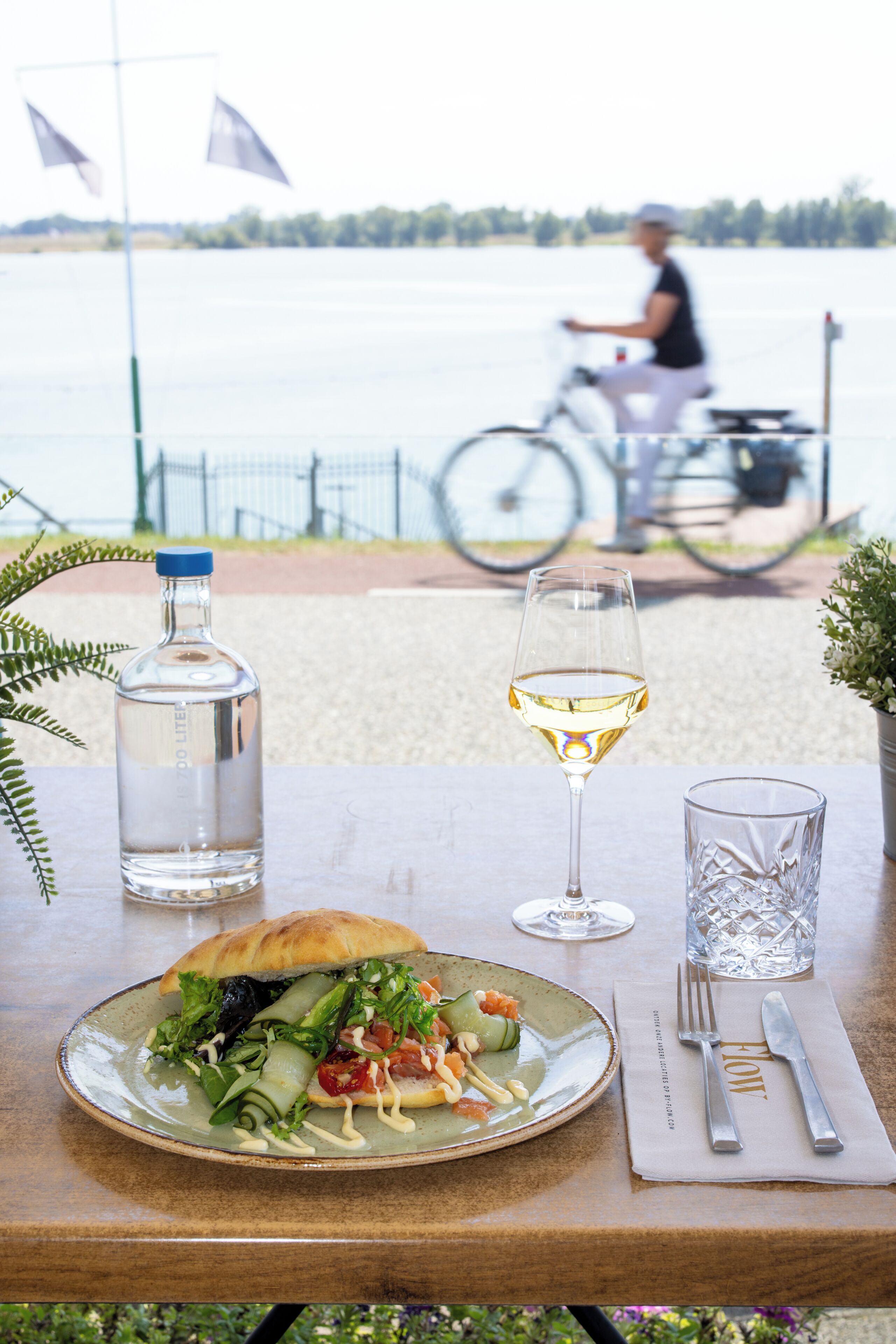 Et bord med et måltid, et glas hvidvin, en vandflaske og et glas vand.