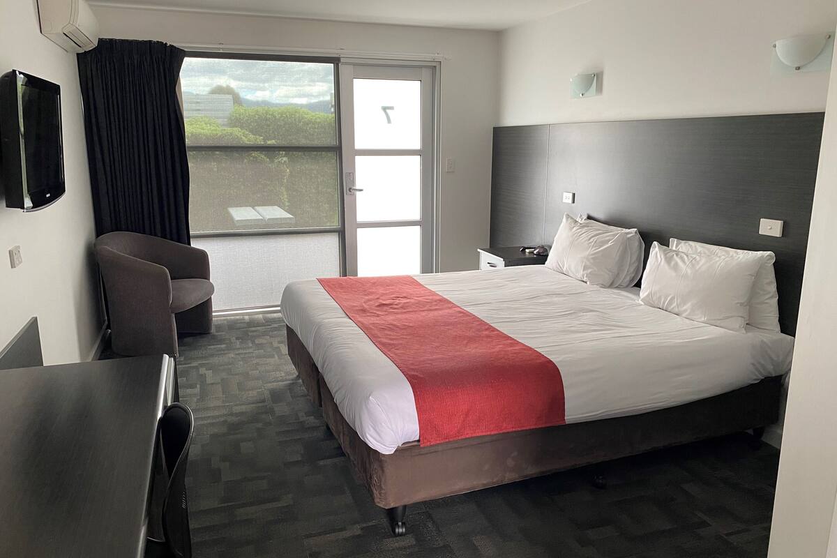 A hotel room with a bed, a desk, a chair, a TV, and a window with curtains.