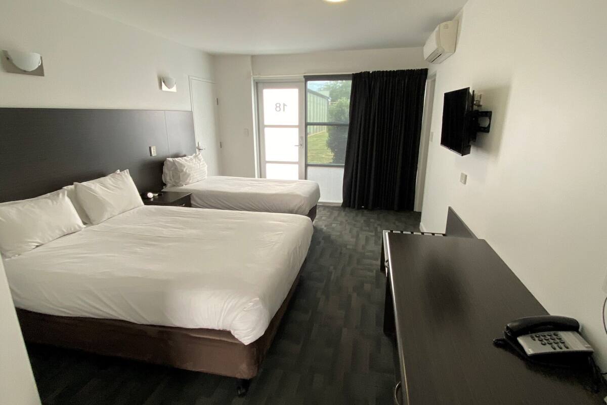 A hotel room with two beds, a desk, a telephone, and a television on the wall.