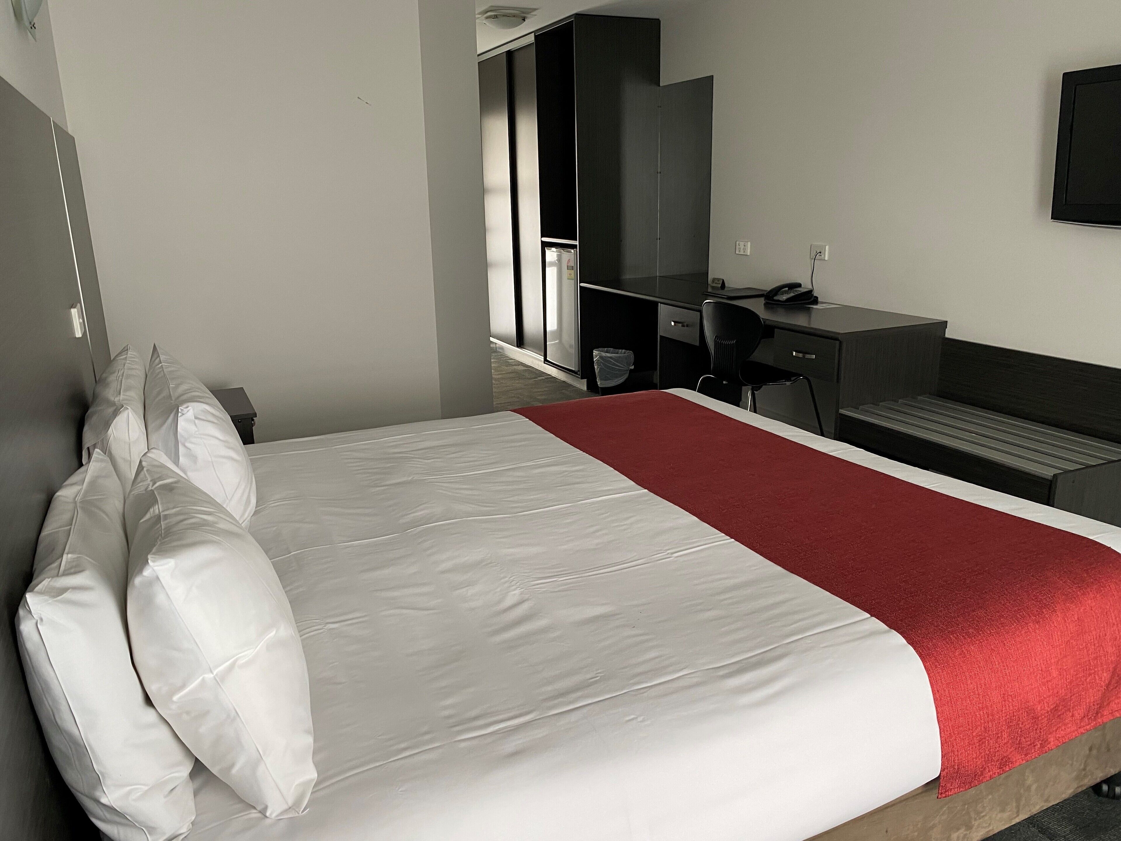 A hotel room with a bed, a desk, a chair, and a TV on the wall.