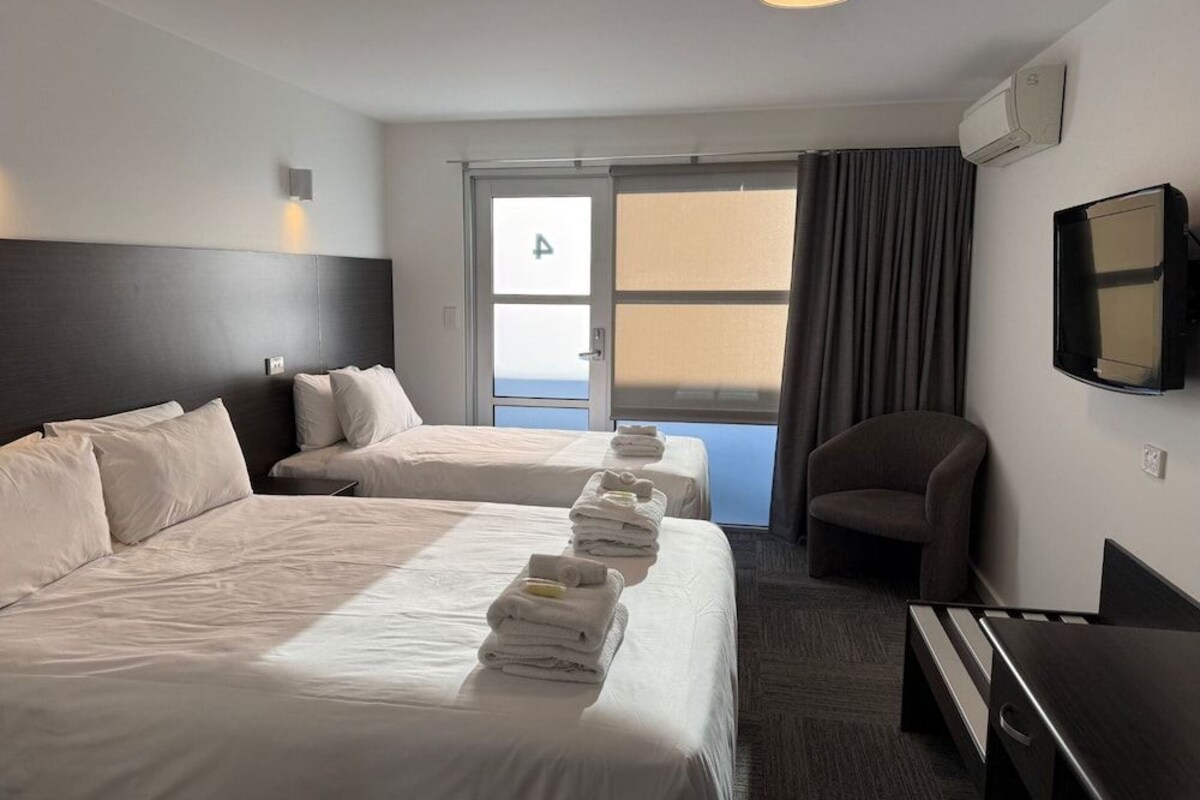 A hotel room with two beds, a desk, a chair, a TV, and a window with curtains.