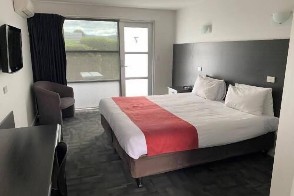 A hotel room with a bed, a desk, a chair, a TV, and a window with curtains.