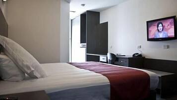 Ett hotellrum med en säng, ett skrivbord, en stol, en tv och en garderob.