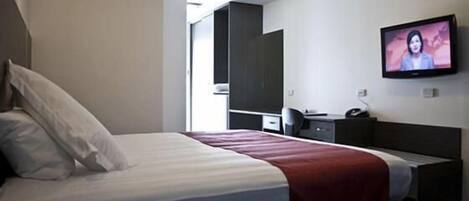 Ein Hotelzimmer mit Bett, Schreibtisch, Stuhl, Fernseher und Kleiderschrank.