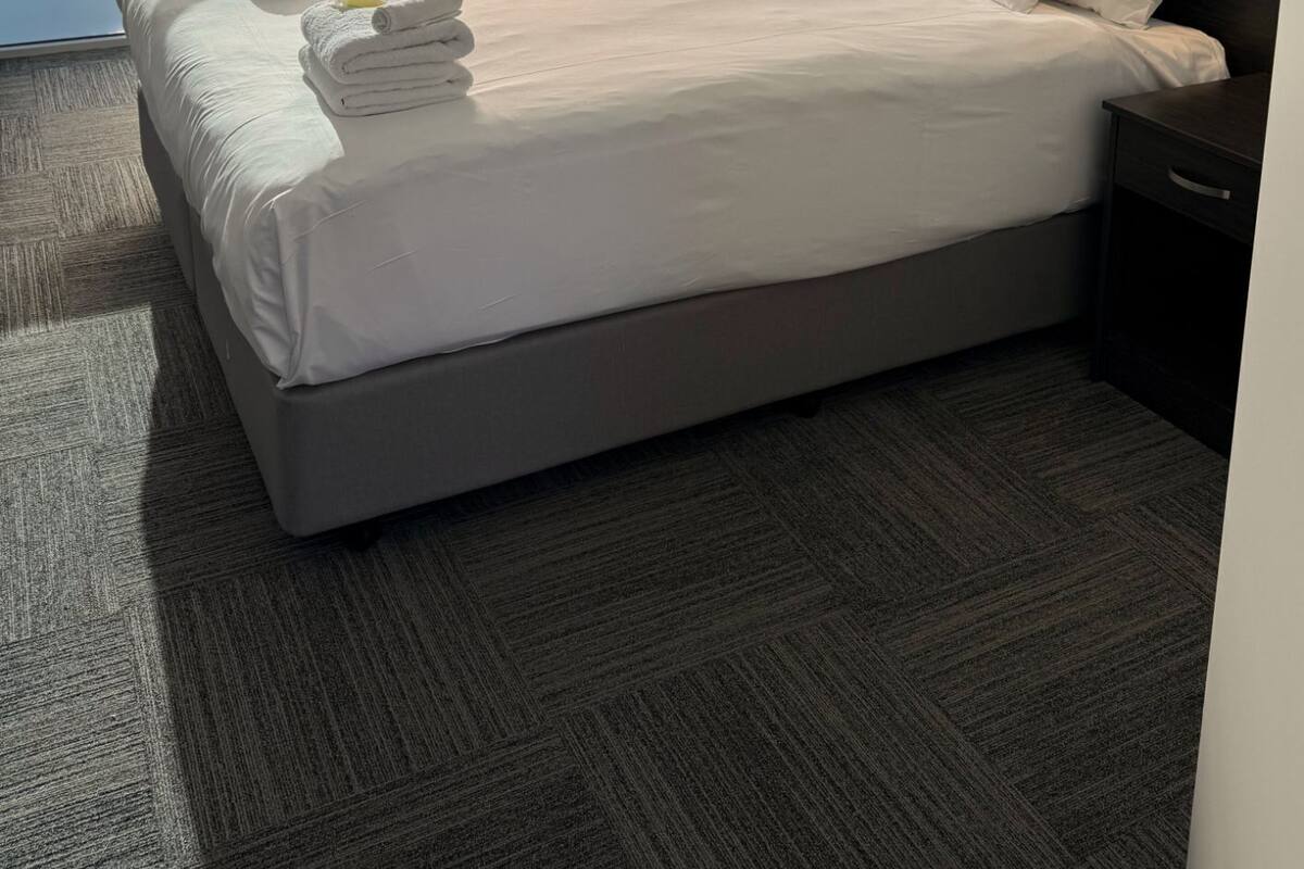 A hotel room with a large bed, a dark headboard, a nightstand, and a view through a sliding door.