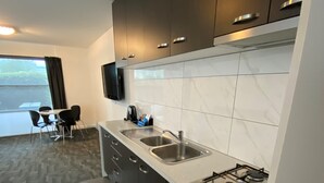 Et moderne køkken med mørke skabe, en gasblus og en indbygget ovn. Et spiseområde med et bord og stole kan ses igennem en åben dør.