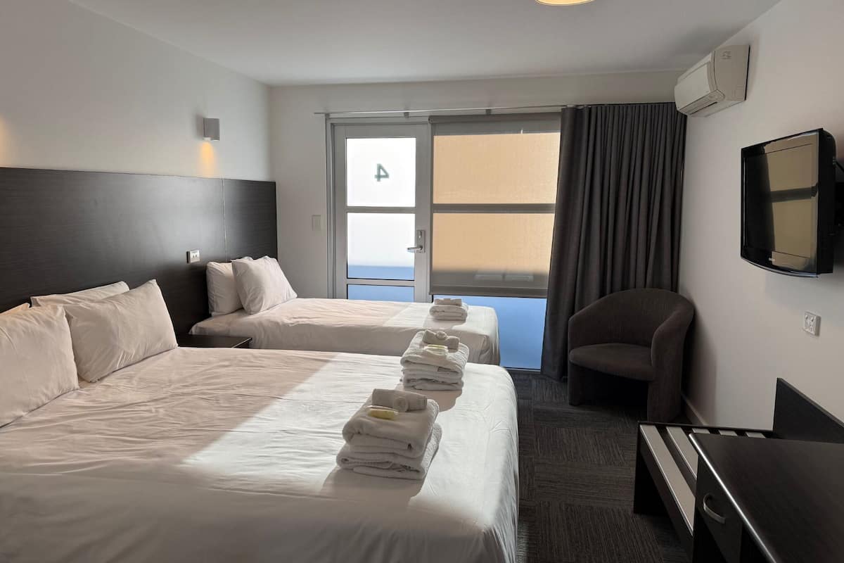 A hotel room with two beds, a desk, a chair, a TV, and a window with curtains.