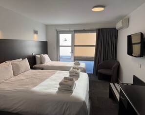 A hotel room with two beds, a desk, a chair, a TV, and a window with curtains. - Brighton Hotel Motel (Brighton)