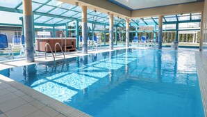 Una piscina interior con agua azul cristalina, techo de cristal y sillas azules alrededor.