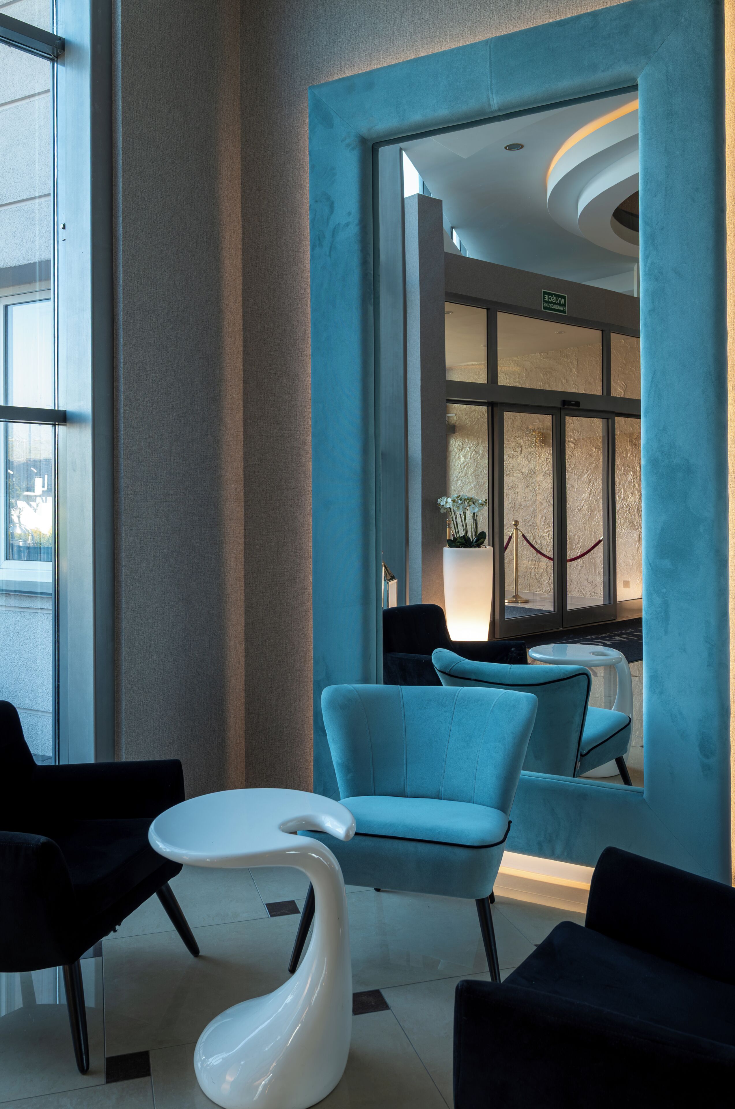 A modern lobby with a seating area, a unique white chair, and a view through a glass door.