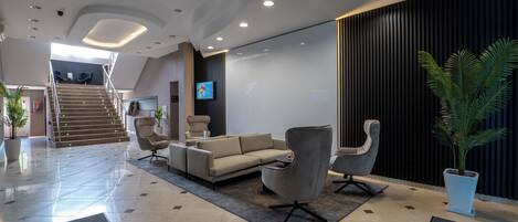 A modern lobby with a sofa, armchairs, a staircase, and a TV screen.