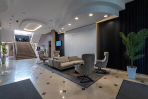 A modern lobby with a sofa, armchairs, a staircase, and a TV screen.