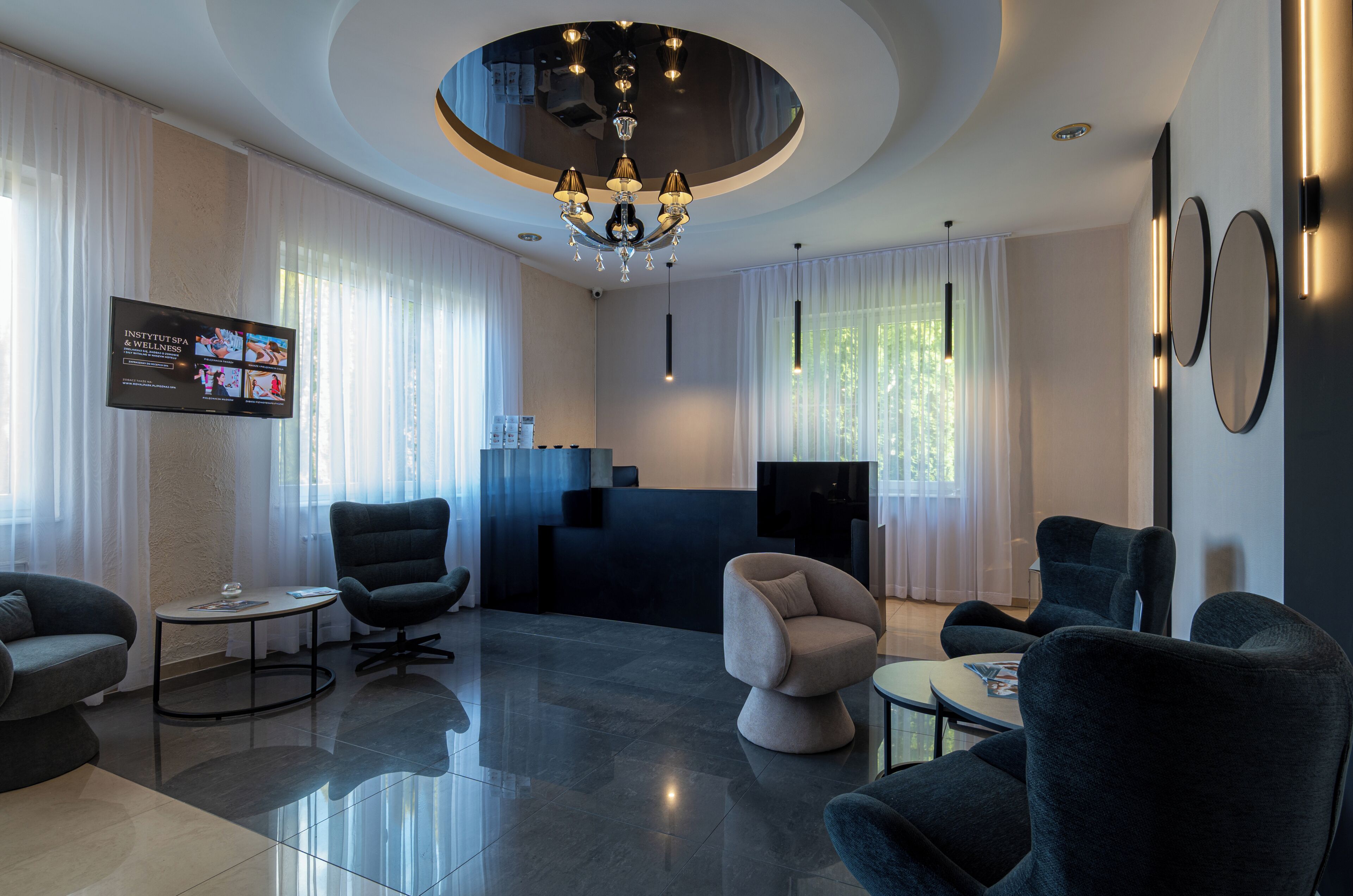 A modern hotel lobby with a reception desk, seating area, and a television displaying wellness content.