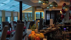 Interior moderno de restaurante con techos altos, luminarias esféricas reflectantes y una zona de bar con una vitrina de copas de vino.