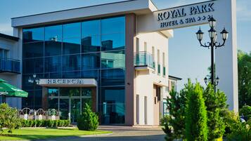 Um hotel moderno com área de recepção, fachada de vidro e uma placa indicando ser o Royal Park Hotel & Spa.