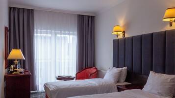 Een hotelkamer met twee bedden, een rode stoel, een nachtkastje met een lamp en een raam met gordijnen.