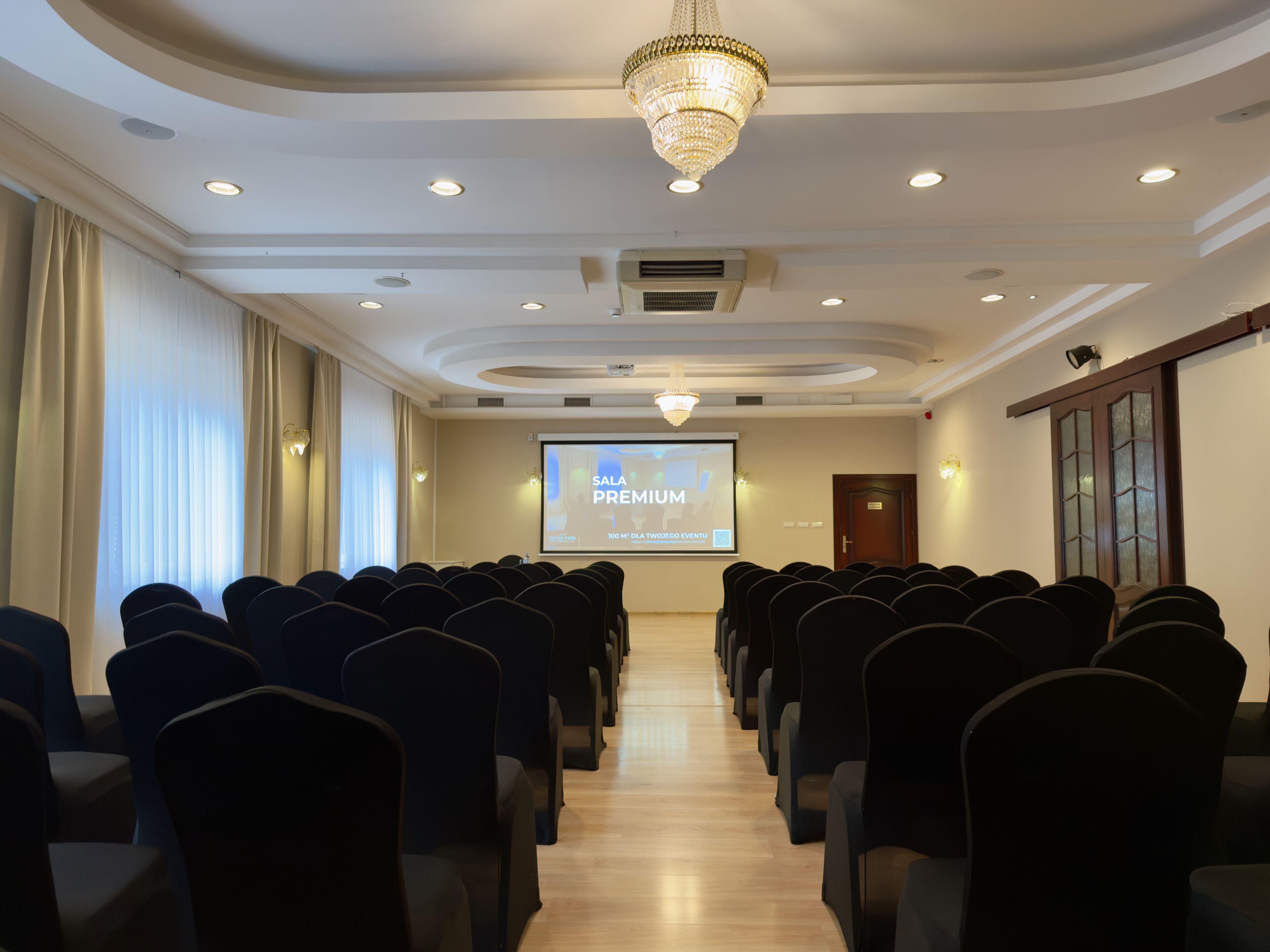 A conference room with rows of chairs, a projector screen, and a chandelier.