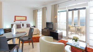 Quarto de hotel moderno com cama, televisão, área de refeições e varanda com vista.