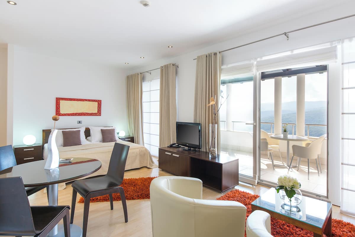 Une chambre d’hôtel moderne équipée d’un lit, d’une télévision, d’un coin repas et d’un balcon avec vue.