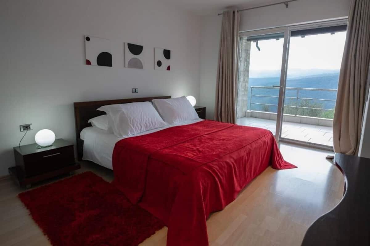 Une chambre à coucher avec un lit, une table de chevet, un tapis rouge et une grande fenêtre donnant sur un beau paysage.
