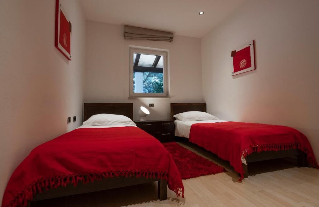 A bedroom with two beds, a window, and a nightstand.