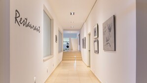 Um corredor moderno de hotel com uma área de recepção no final, apresentando uma escadaria e obras de arte emolduradas nas paredes.