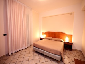A hotel room with a bed, a nightstand, a lamp, and a curtain.