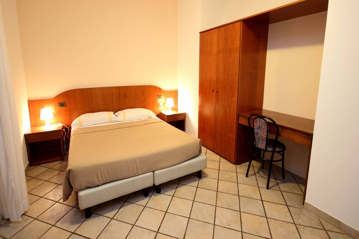 A hotel room with a bed, bedside lamps, a desk, and a chair.