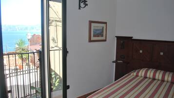 Una camera da letto con un letto, un comodino, un armadio in legno, un quadro appeso al muro e un balcone con vista sul mare.