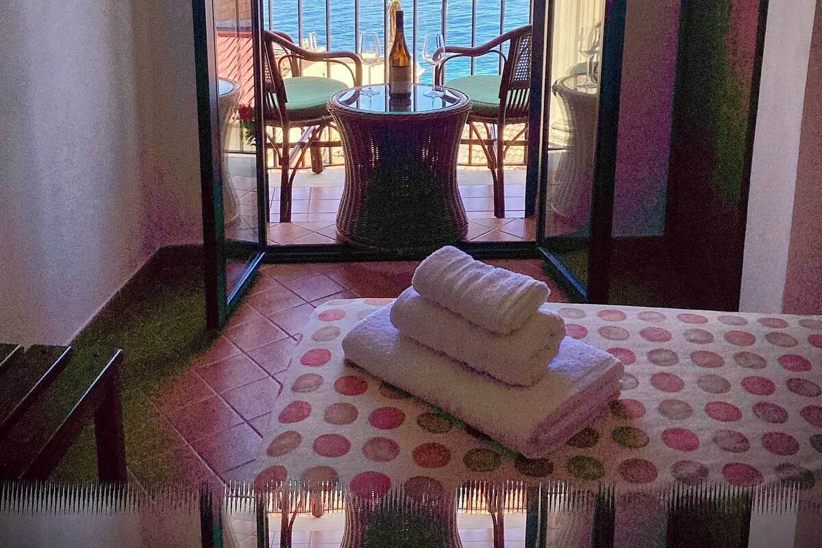 A balcony with a table and chairs, a view of the sea, and a bed with a polka dot bedspread.