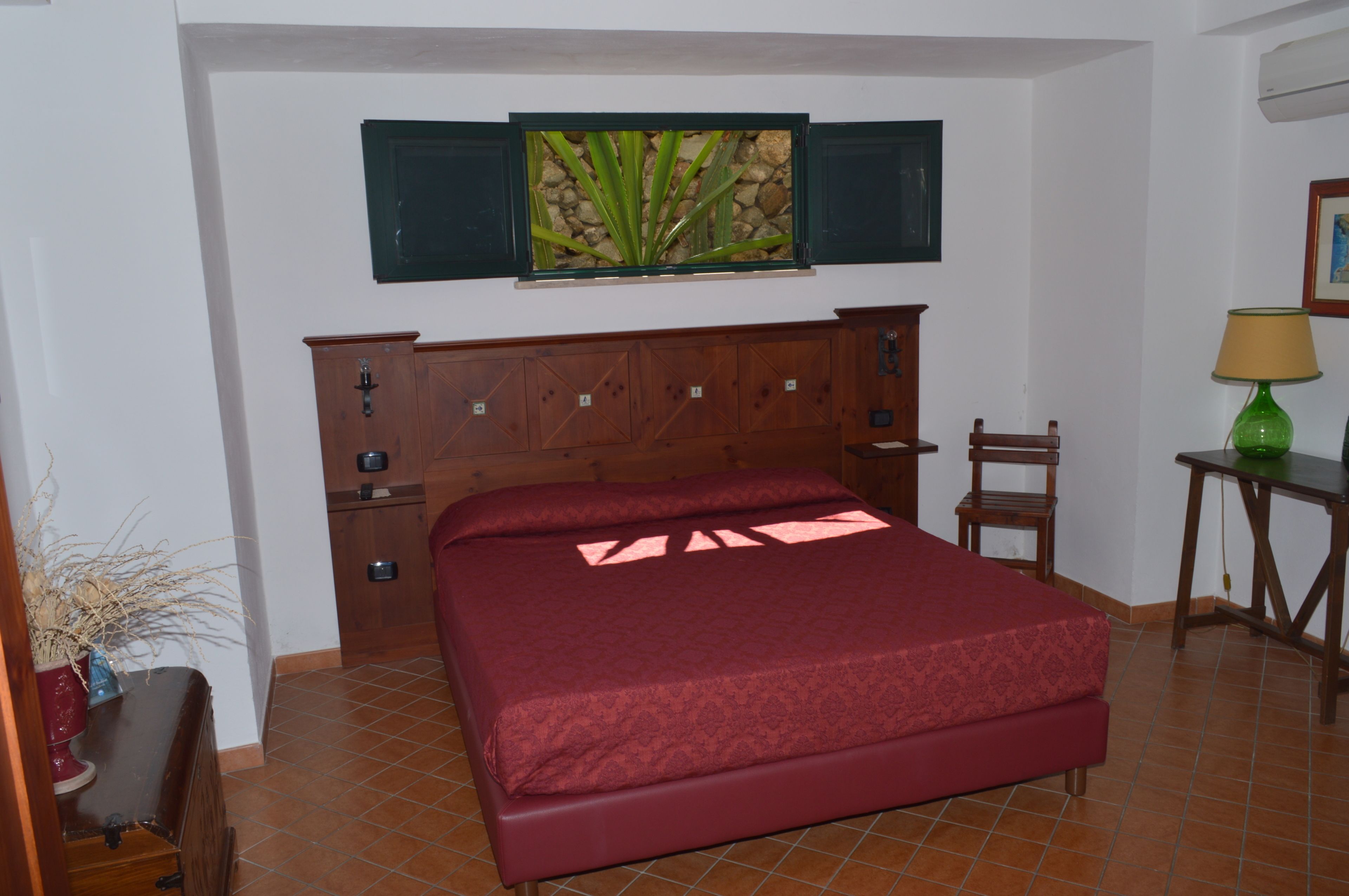 A bedroom with a wooden bed, a nightstand, a chair, a small table, and a wall-mounted shelf.
