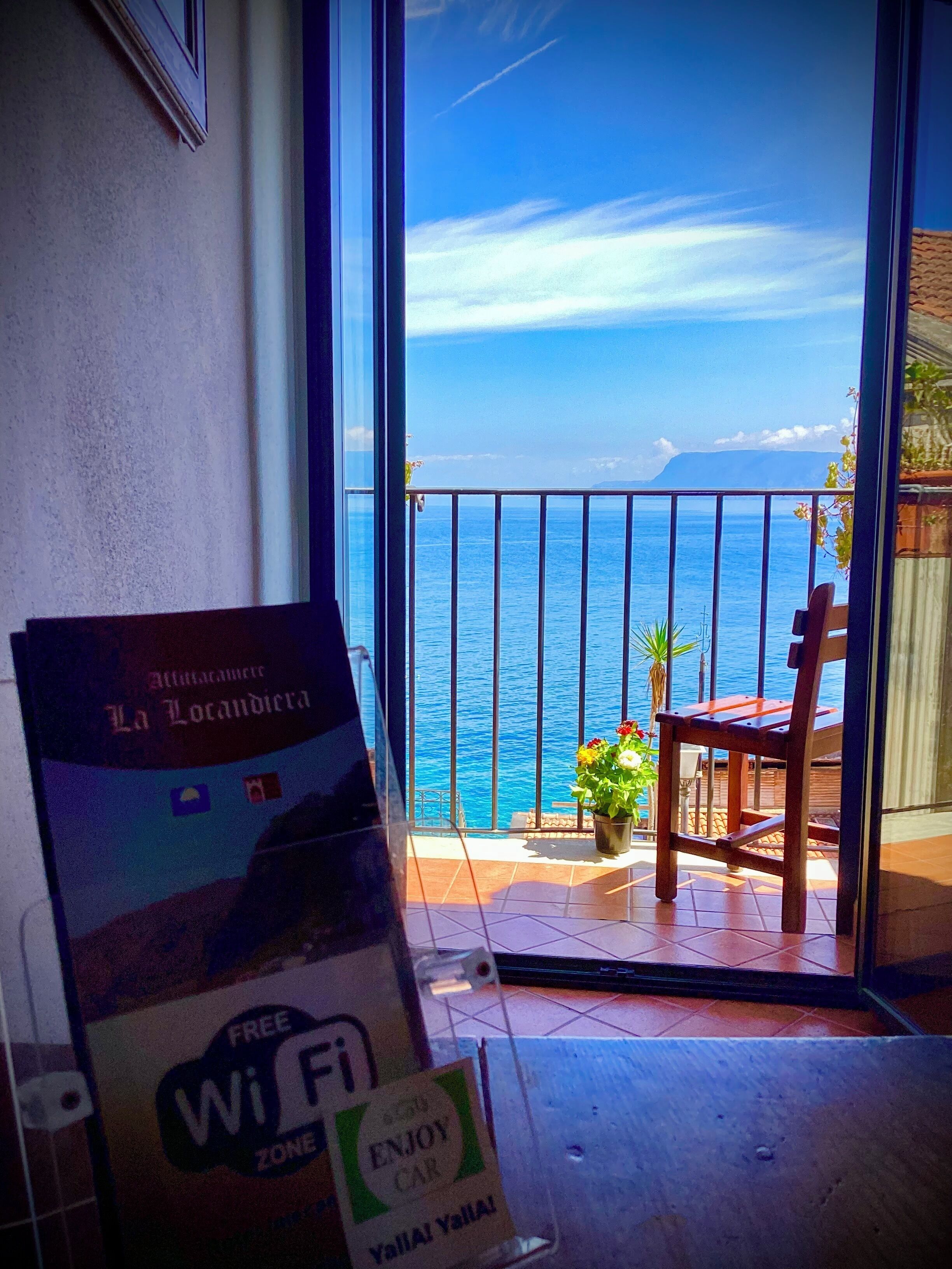 A balcony with a view of the sea, a chair, a potted plant, and a sign indicating a free Wi-Fi zone.