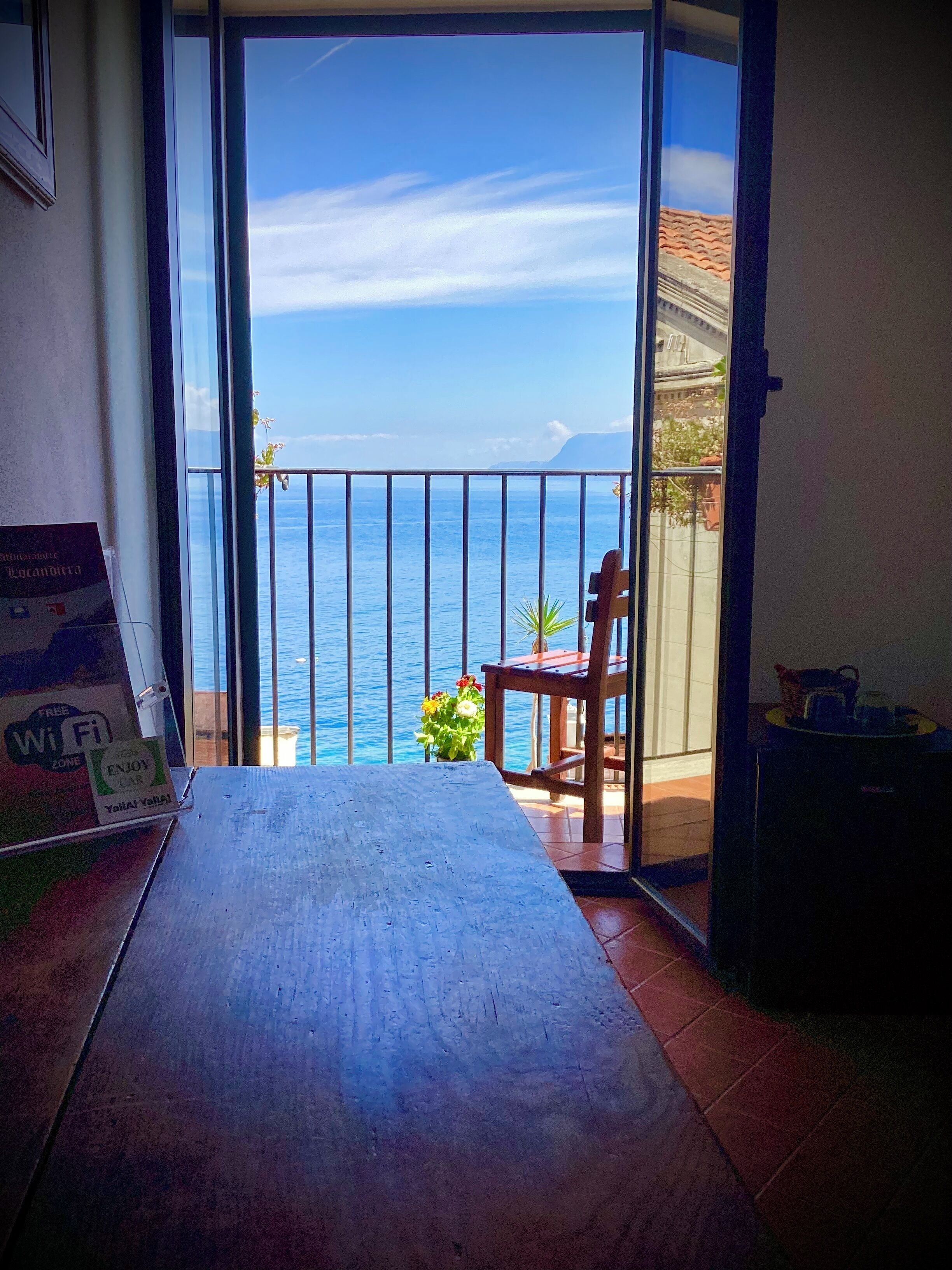 Un balcón con vista al mar, una silla, una mesa y un letrero que indica Wi-Fi gratuito.