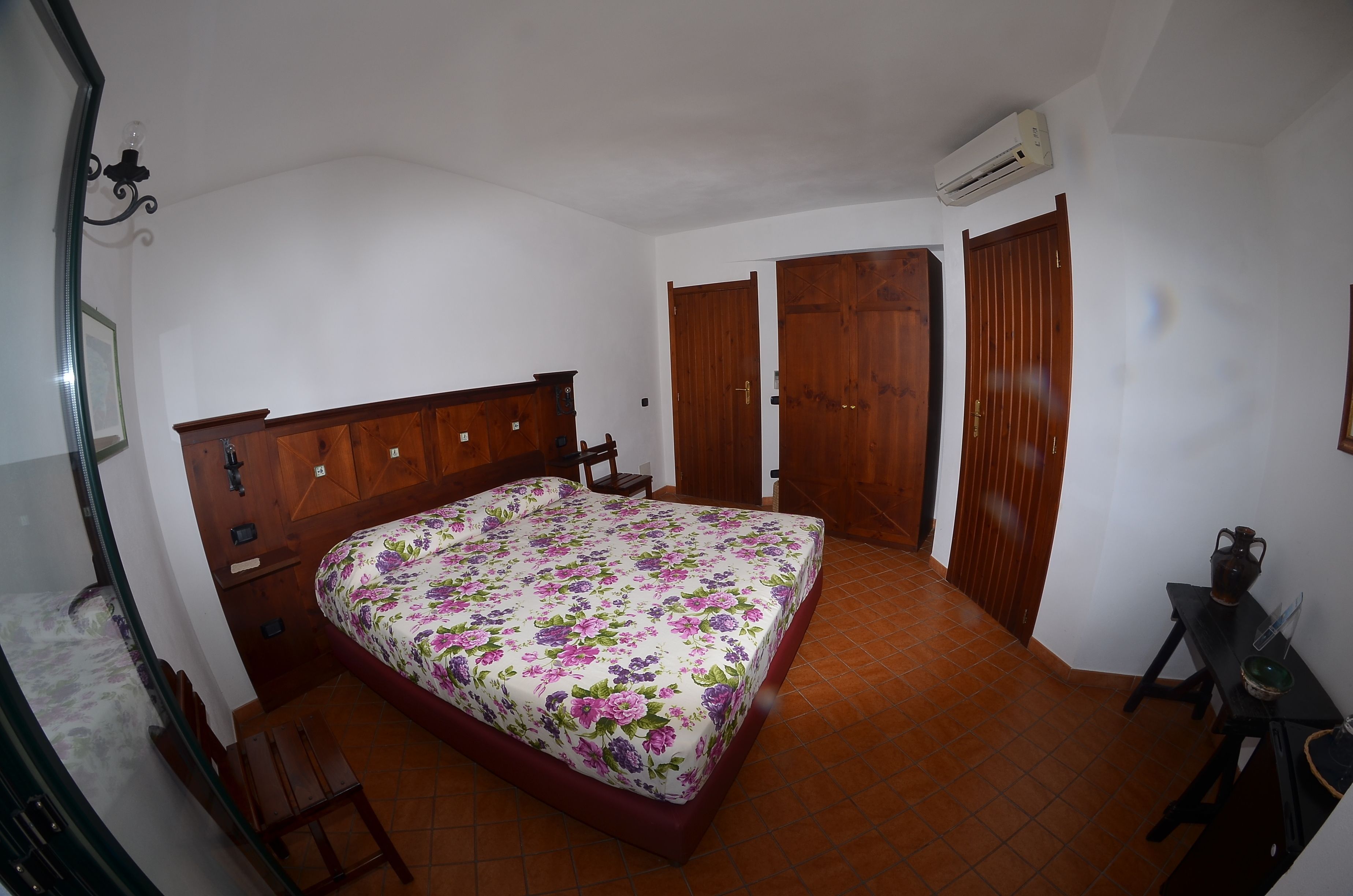 A bedroom with a floral bedspread, wooden wardrobe, and an air conditioning unit.