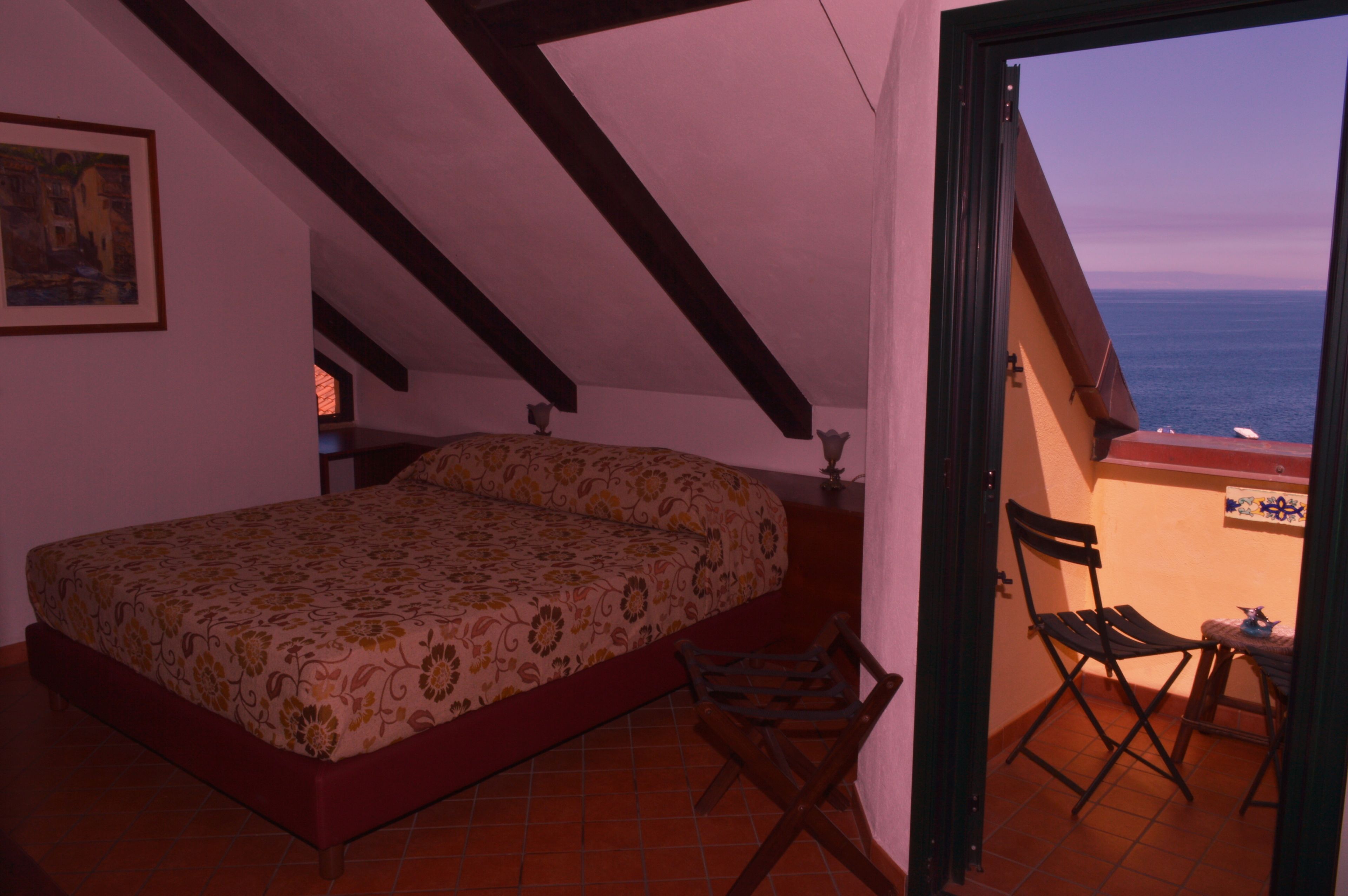 Un dormitorio con cama, una silla y vista al mar a través de una puerta abierta.
