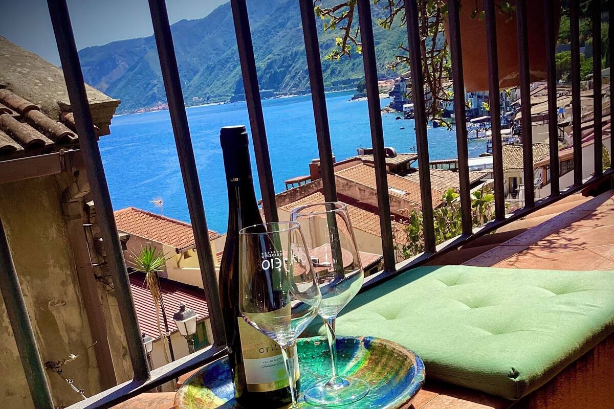 A balcony with a view of the sea, a bottle of wine, and two glasses.