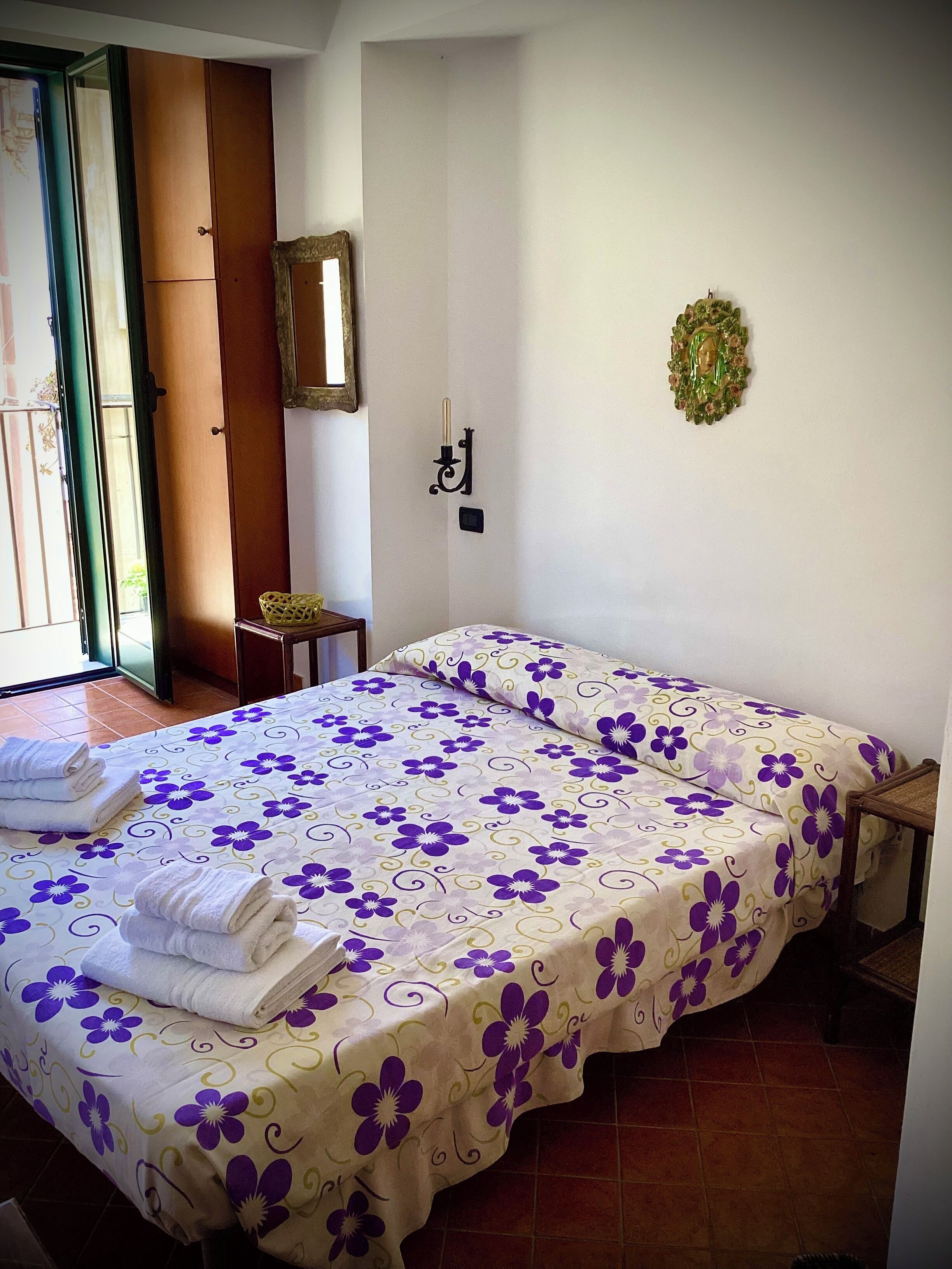 A room with a bed, a small table, a chair, a mirror, and a door.