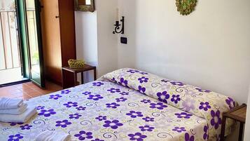 A room with a bed, a small table, a chair, a mirror, and a door.