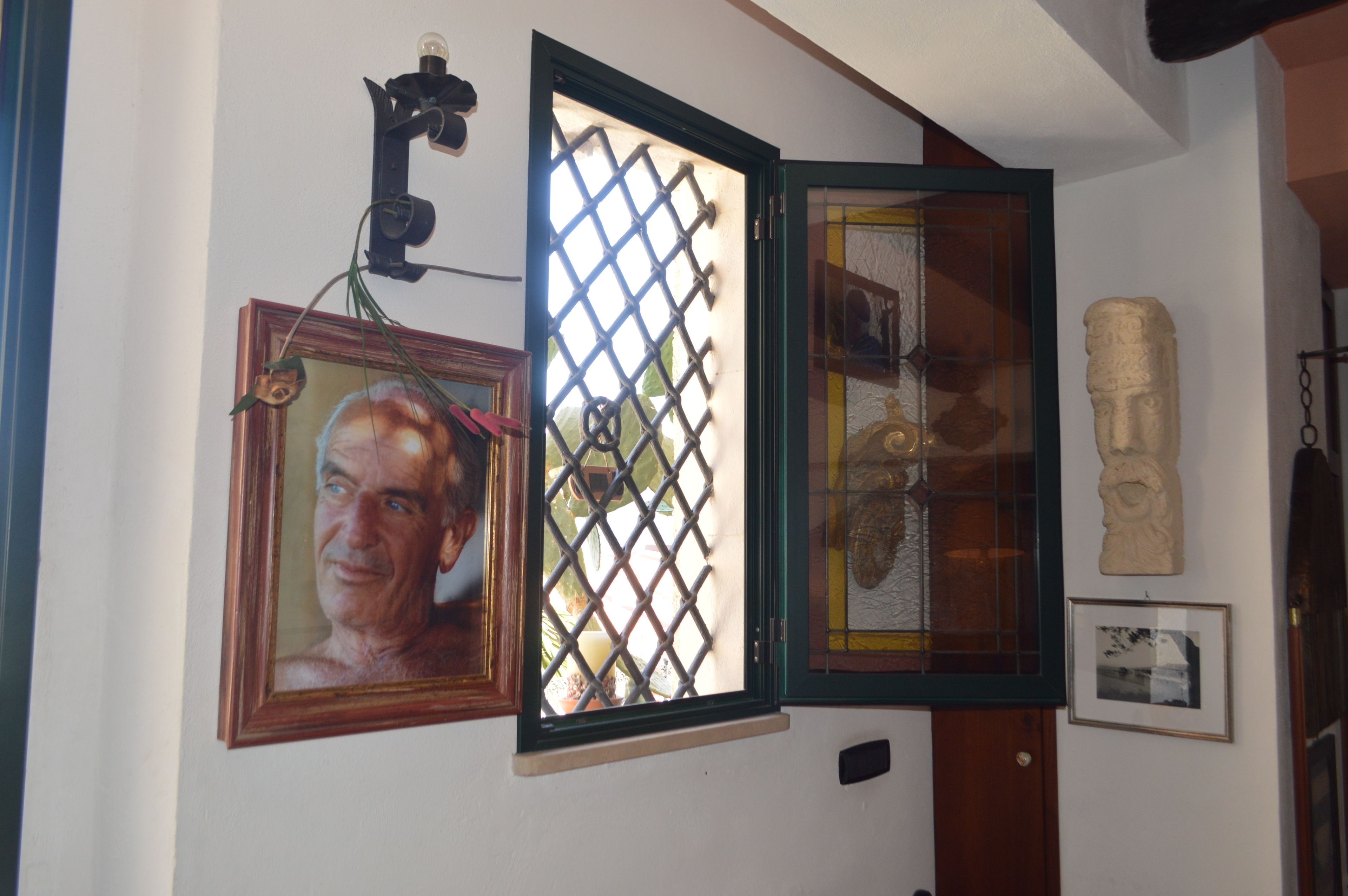 A room with a wooden door, a window with a metal grid, a framed picture, and a stone sculpture on the wall.
