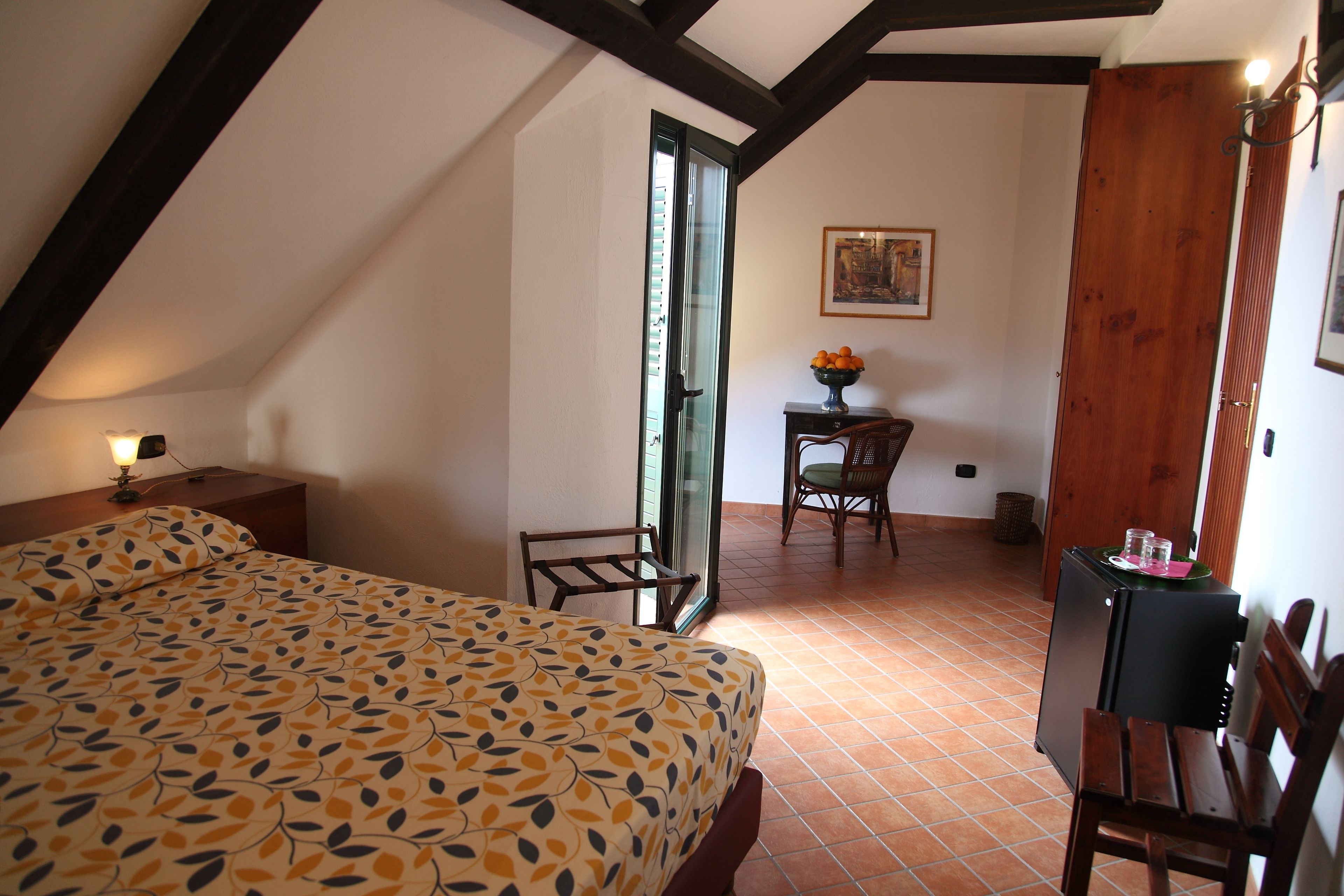 A bedroom with a bed, a desk, a chair, and a small table with a vase of flowers.