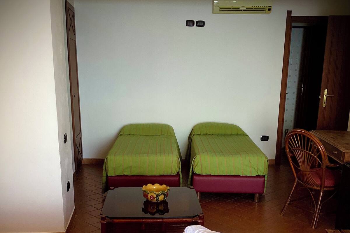A hotel room with two single beds, a wooden table with a vase, a chair, and a large bed with a polka dot cover.
