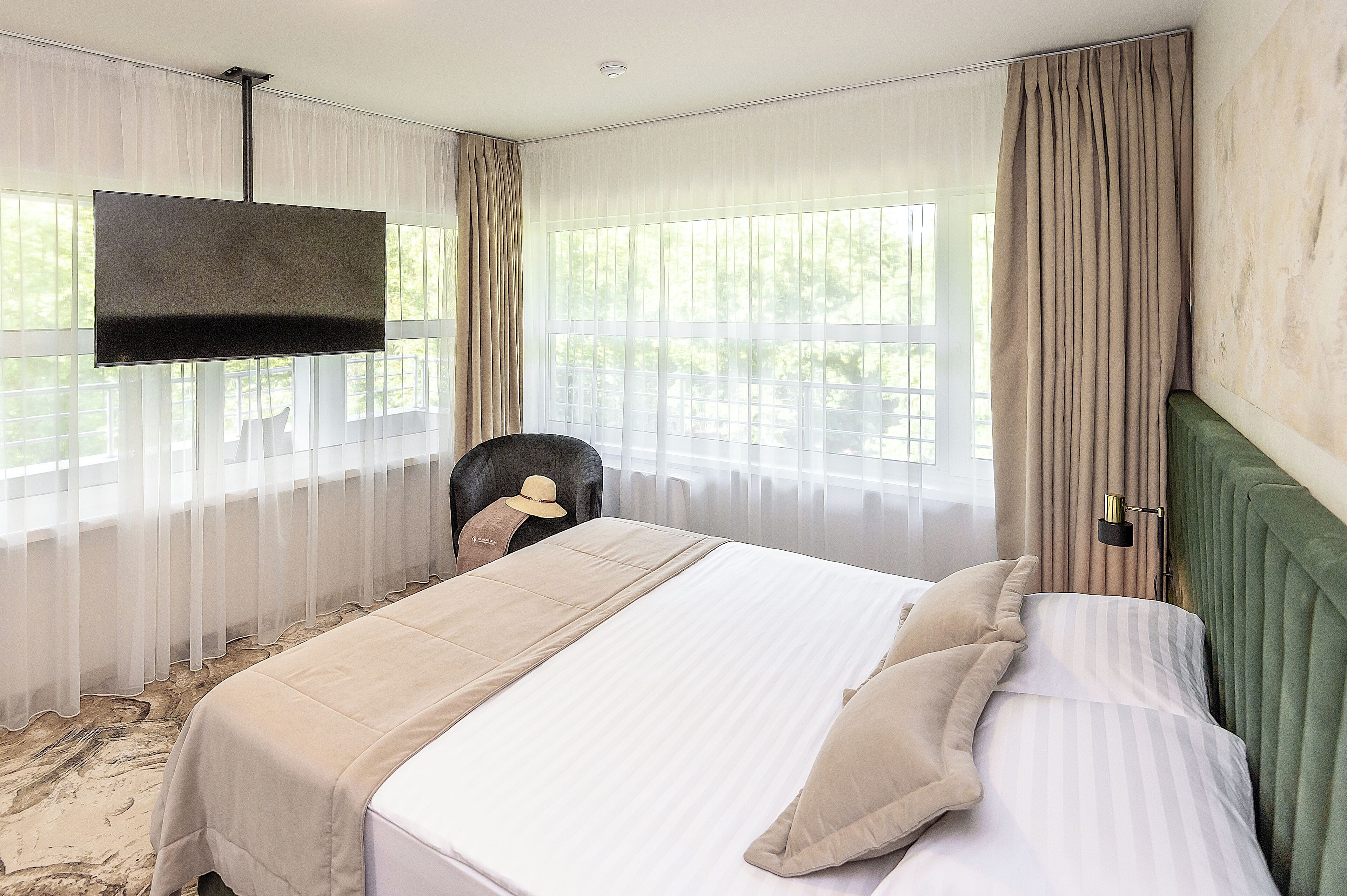 A hotel room with a bed, a TV mounted on the wall, and a chair.