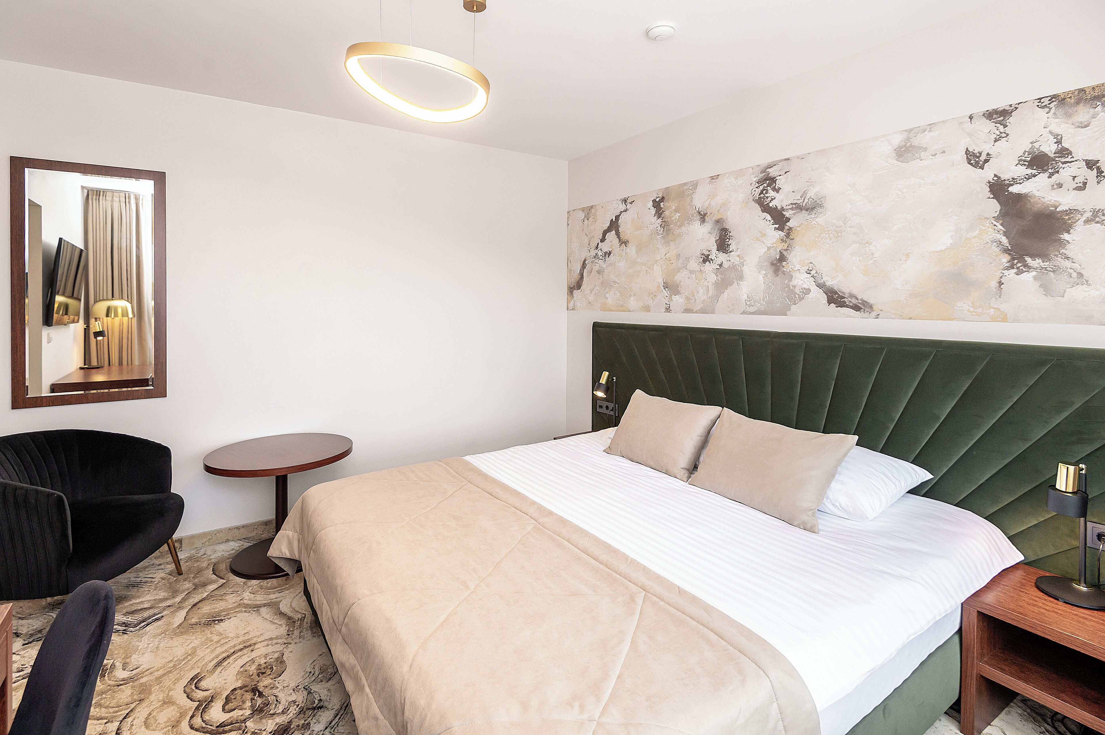 Una habitación de hotel moderna con una cama grande, una mesita redonda, una silla y un cuadro en la pared.
