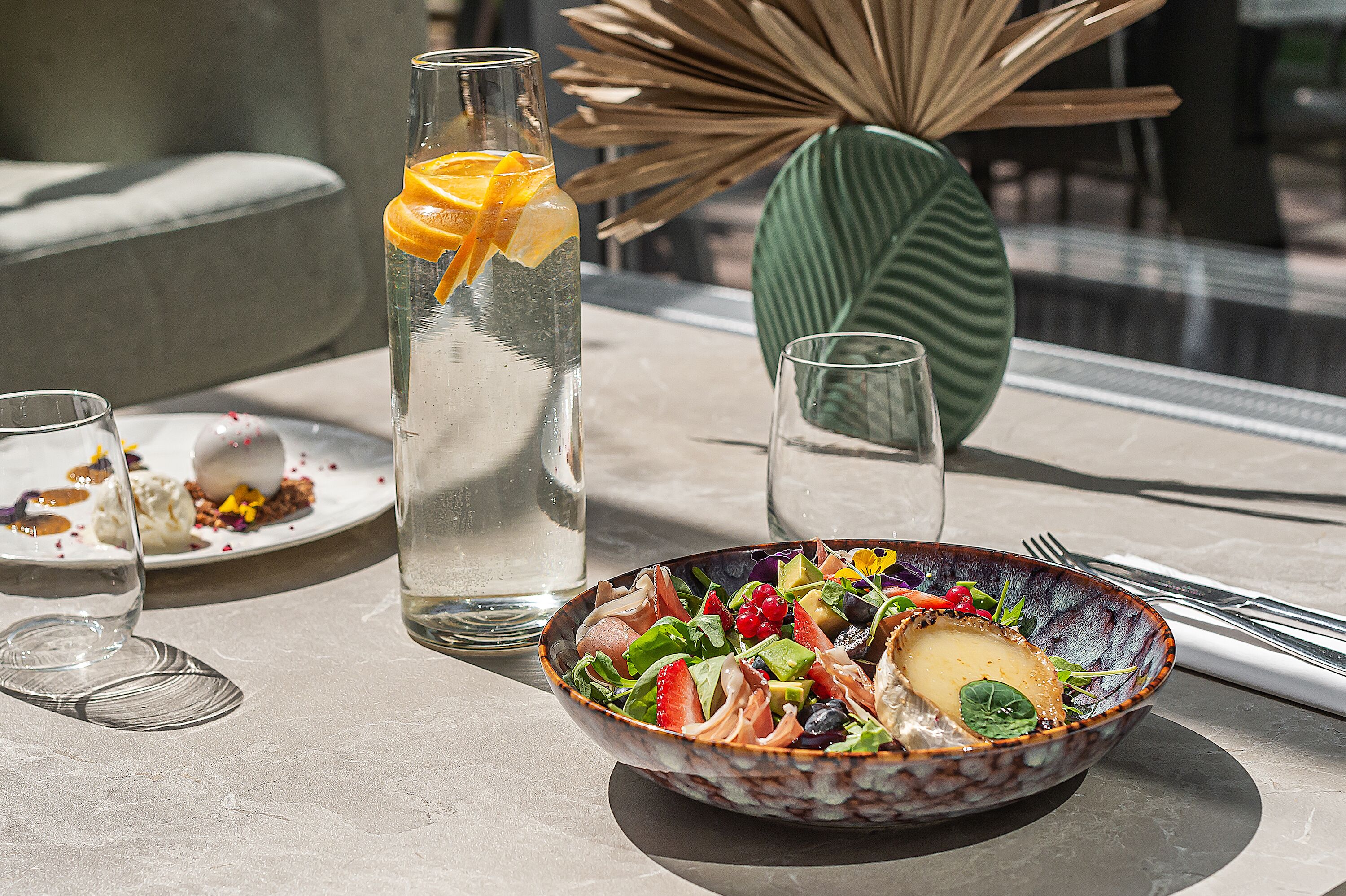 A table with a bowl of salad, a glass of water, and a bottle of water with an orange slice.