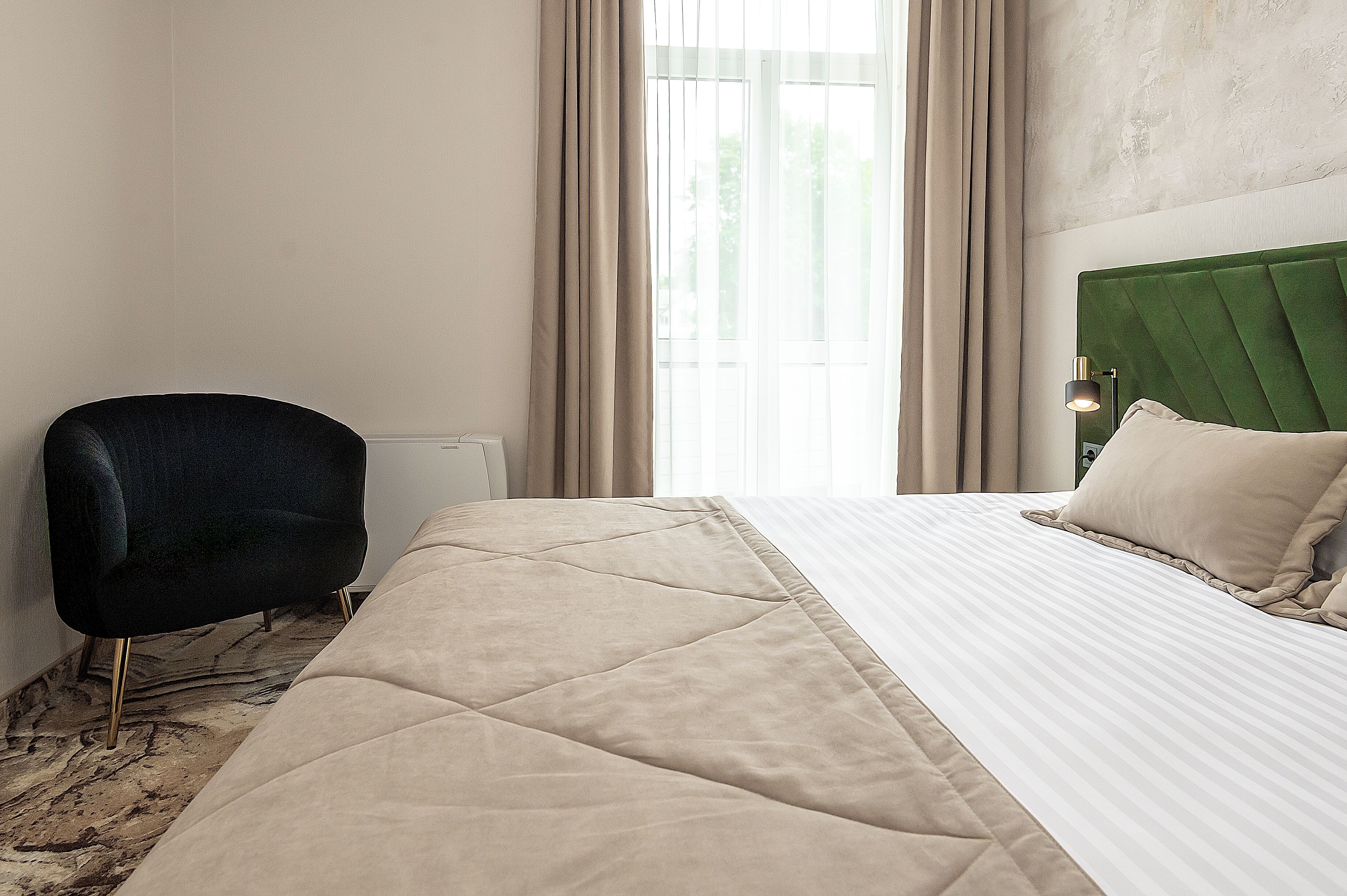 Quarto de hotel com uma cama, uma cadeira e uma janela com cortinas.
