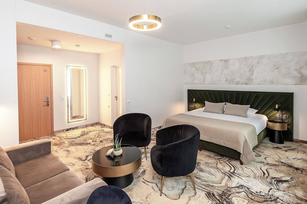 A hotel room with a bed, two armchairs, a coffee table, and a round ceiling light.
