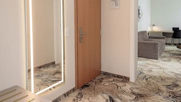 A hotel room with a wooden door, a desk with a chair, a sofa, and a patterned carpet.